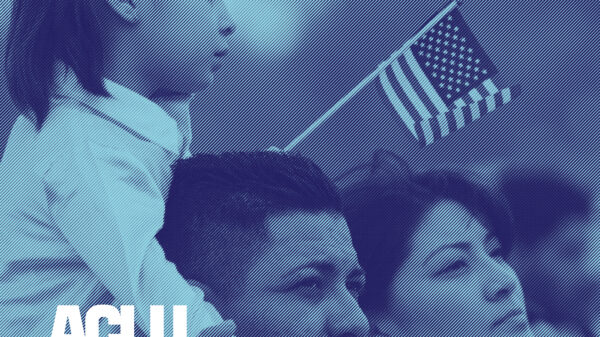Young girl holding a small American flag and sitting on her dad's shoulder. Her mom is standing next to them.
