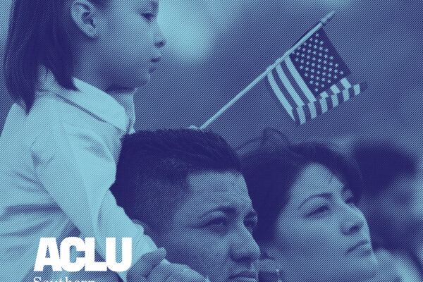 Young girl holding a small American flag and sitting on her dad's shoulder. Her mom is standing next to them.