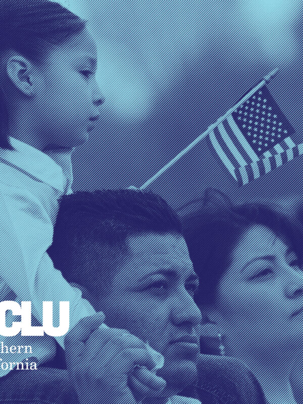 Young girl holding a small American flag and sitting on her dad's shoulder. Her mom is standing next to them.