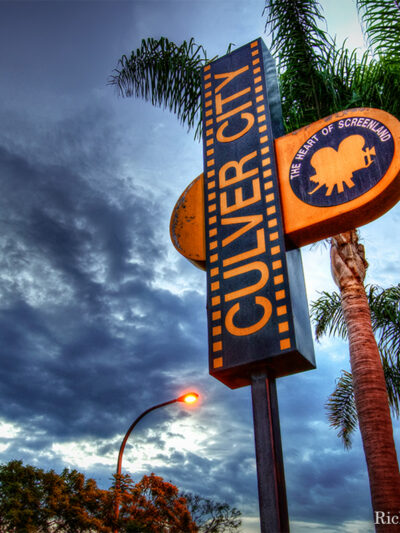 Culver City sign in front of palm tree with sky and clouds in the background