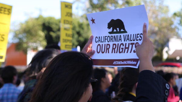 Woman in crowd holding a sign above her head that reads: California values our rights