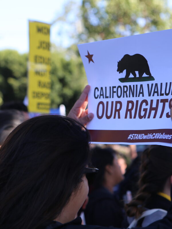 Woman in crowd holding a sign above her head that reads: California values our rights