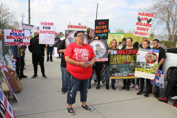 A group of people gathered on the sidewalk holding signs protesting police brutality