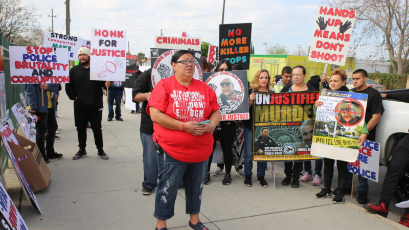 A group of people gathered on the sidewalk holding signs protesting police brutality