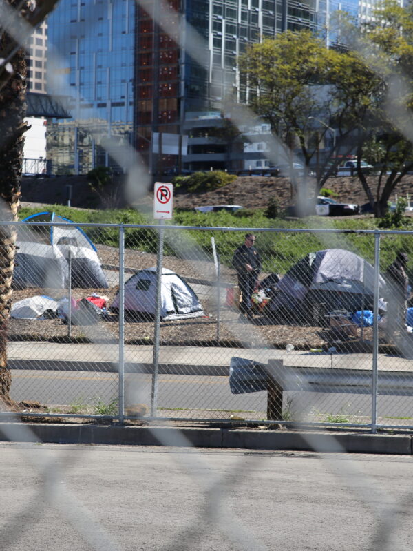 A police officer standing next to a group of tents to the side of a freeway on-ramp
