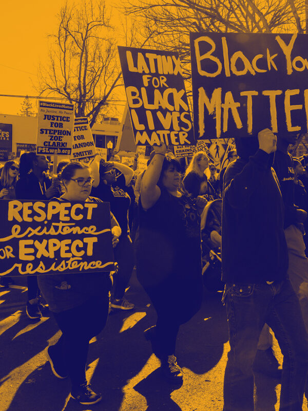 Large group of people protesting, walking down the street holding signs that read "Black Youth Matter," "Latinos for Black Lives Matter," "Respect existence or expect resistance"