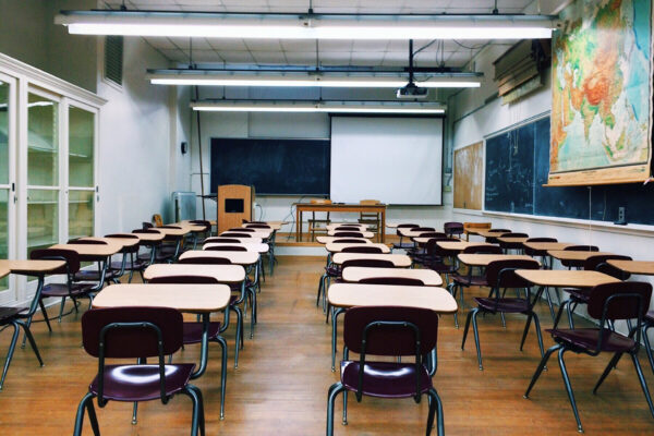 A classroom with five rows of school desks, a blackboard at the far end of the room, and a big world map to the right of the room