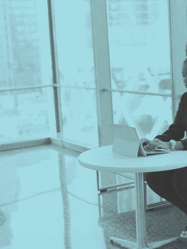 A young Black woman with an afro puff sitting on a sofa, using her laptop at a small table. Image courtesy of #WOCinTech Chat.