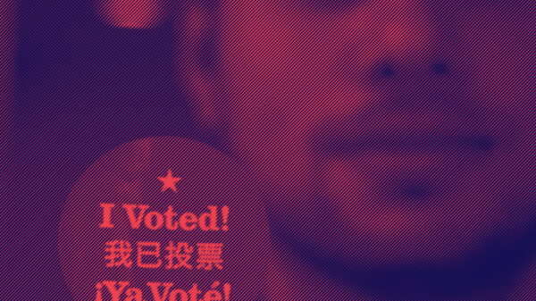 Man holding up a round sticker with text that reads: I voted!