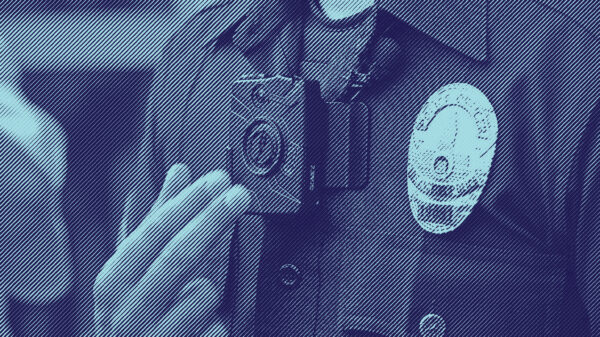 Close up photo of a police man wearing a body camera near his lapel, next to his police badge