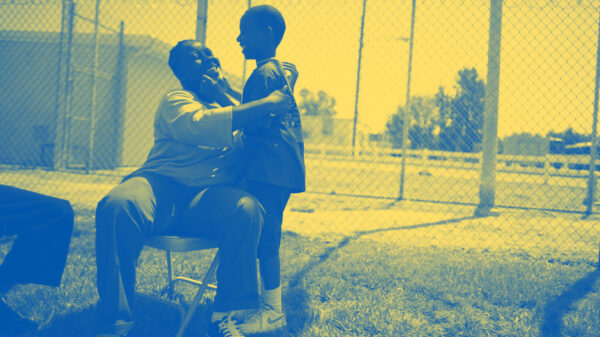 A woman sitting on a chair in a prison courtyard, embracing her young son