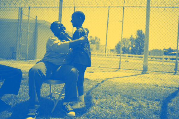 A woman sitting on a chair in a prison courtyard, embracing her young son