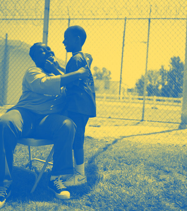 A woman sitting on a chair in a prison courtyard, embracing her young son
