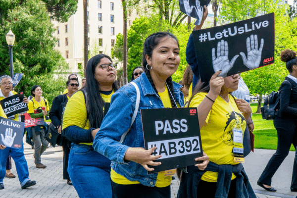 A group of young people wearing matching yellow shirts holding posters in favor of AB 392. They are marching to the California state Capitol.