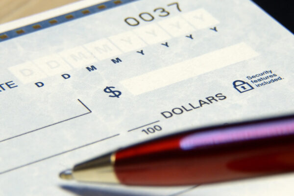 a blank check in the background, a pen in the foreground