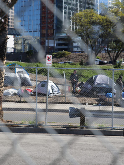 A police officer standing next to a group of tents to the side of a freeway on-ramp