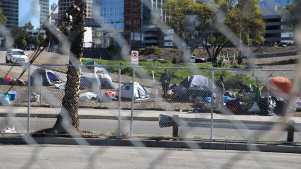 A police officer standing next to a group of tents to the side of a freeway on-ramp