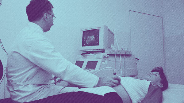 A woman lying on an exam table, a male doctor performing an ultrasound by placing a wand over her abdominal area
