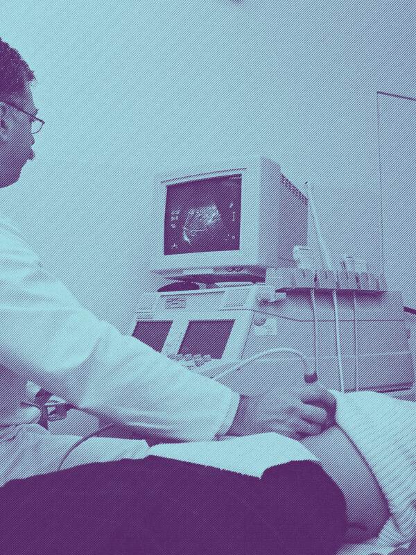 A woman lying on an exam table, a male doctor performing an ultrasound by placing a wand over her abdominal area
