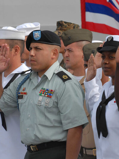 Sailors and Marines with right hands raised taking the oath of citizenship aboard the USS Cleveland.