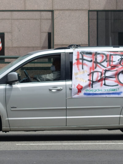 A silver van with a large hand-made sign on the side of the van that reads: Free the People, Check the Sheriff