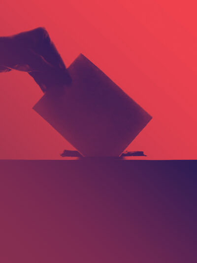 A silhouette of a hand putting a ballot into a ballot box