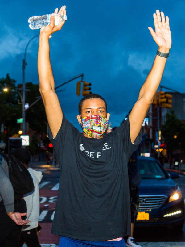 A man at a protest against police violence holding his hands in the air.