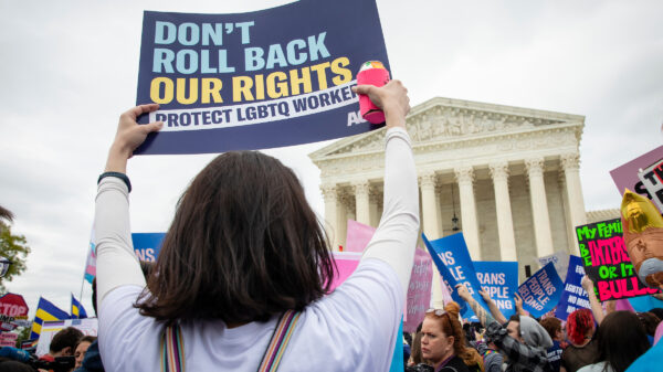 A person at a protest rally in front of the U.S. Supreme court holding a sign that reads: Don't roll back our rights. Protect LGBTQ workers.