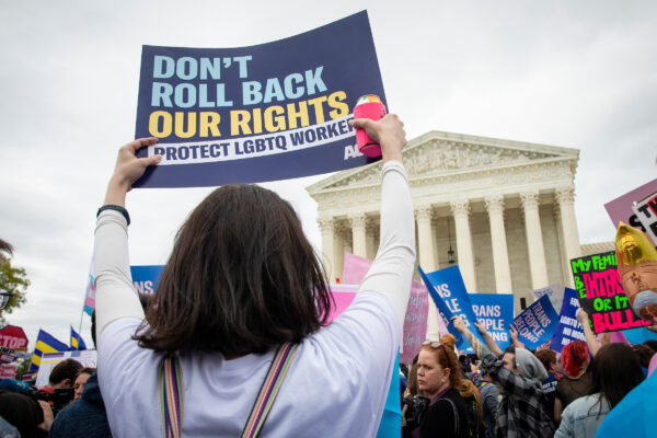 A person at a protest rally in front of the U.S. Supreme court holding a sign that reads: Don't roll back our rights. Protect LGBTQ workers.