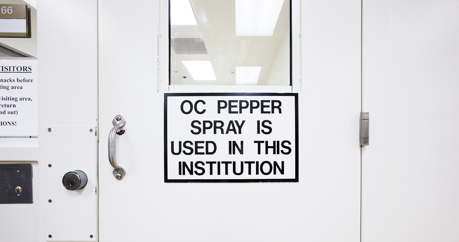 Inside a detention facility, a sign on a door that reads: OC Pepper Spray is Used in This Institution