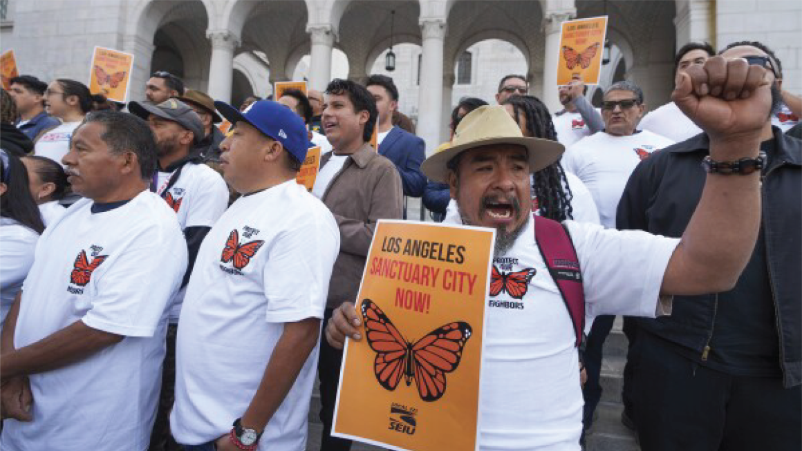 Person with fist raised and rally sign reading Los Angeles Sanctuary City Now