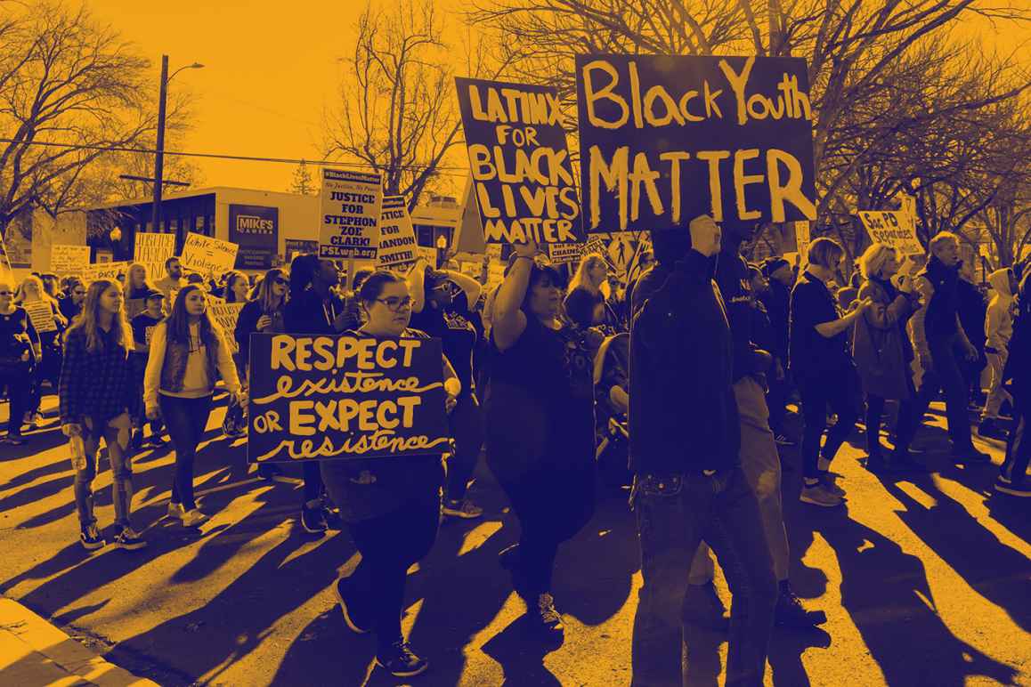 Large group of people protesting, walking down the street holding signs that read "Black Youth Matter," "Latinos for Black Lives Matter," "Respect existence or expect resistance"