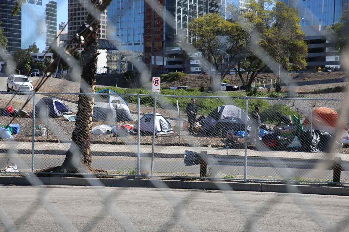 A police officer standing next to a group of tents to the side of a freeway on-ramp