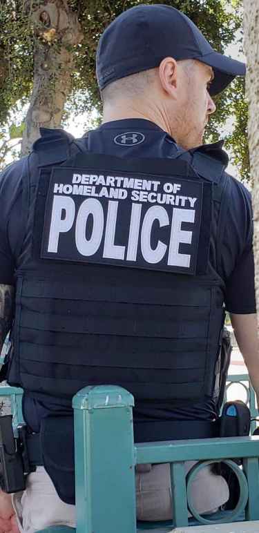 An ICE agent wearing a flak vest with patch that reads Department of Homeland Security POLICE and does not identity the person as an ICE agent