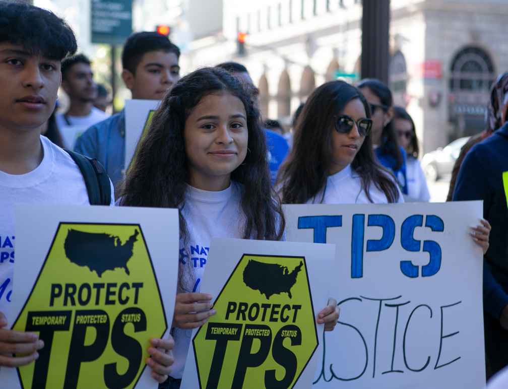 Crista Ramos and TPS rally attendees hold up signs that say, "Protect TPS."