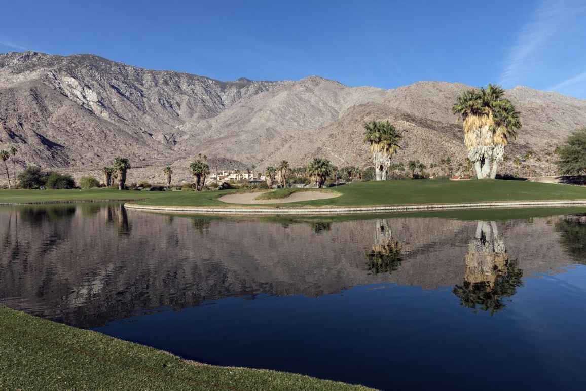 Golf course in Coachella Valley, a pond in the foreground, palm trees and mountain range in the background