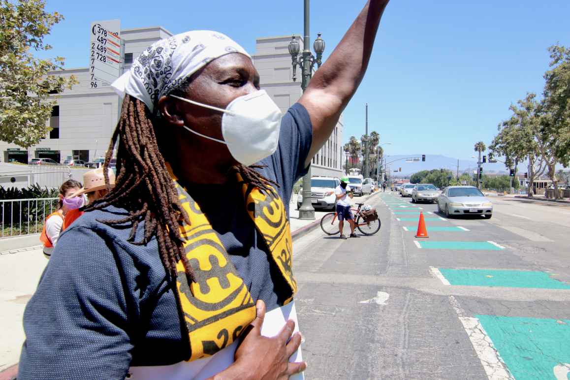 A Black clergy member, wearing a face mask, protesting in the street with their arm raised