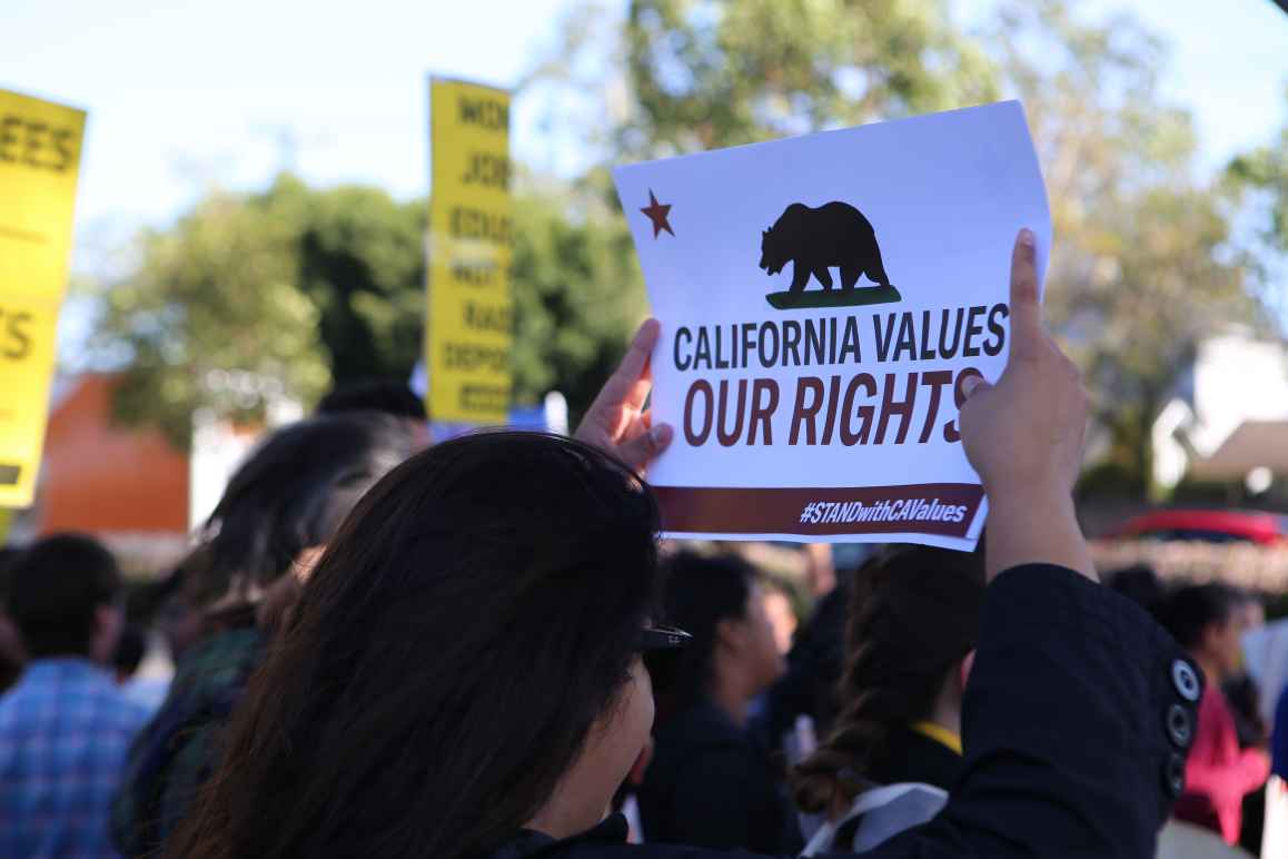 Woman in crowd holding a sign above her head that reads: California values our rights