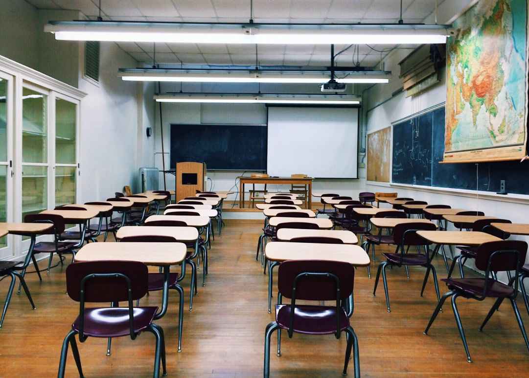 A classroom with five rows of school desks, a blackboard at the far end of the room, and a big world map to the right of the room
