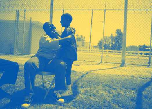 A woman sitting on a chair in a prison courtyard, embracing her young son