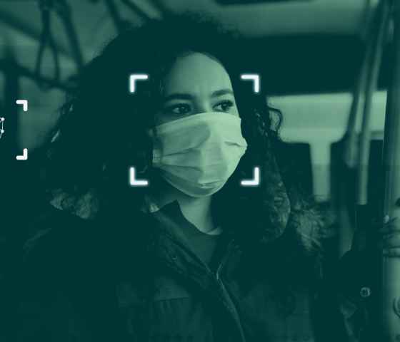 A simulation of facial recognition technology: a photograph of a woman on a public bus wearing a mask with graphics overlayed indicating that the software is scanning her face.