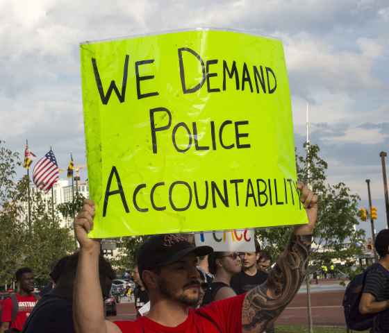 A man holding a hand-written sign that reads "We Demand Police Accountability"