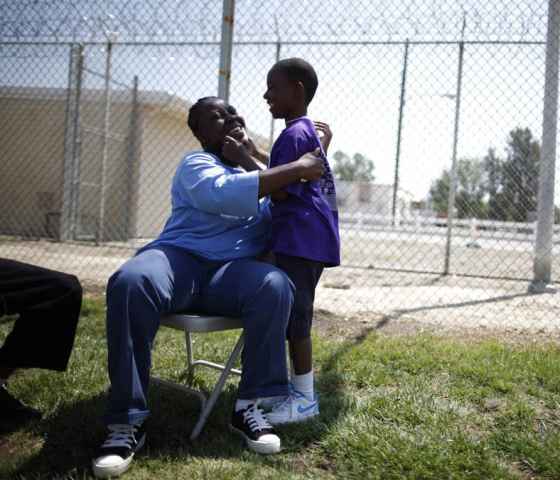 A woman sitting on a chair in a prison courtyard, embracing her young son